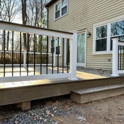 Photo of a new deck with white railing and black balusters with sun shining