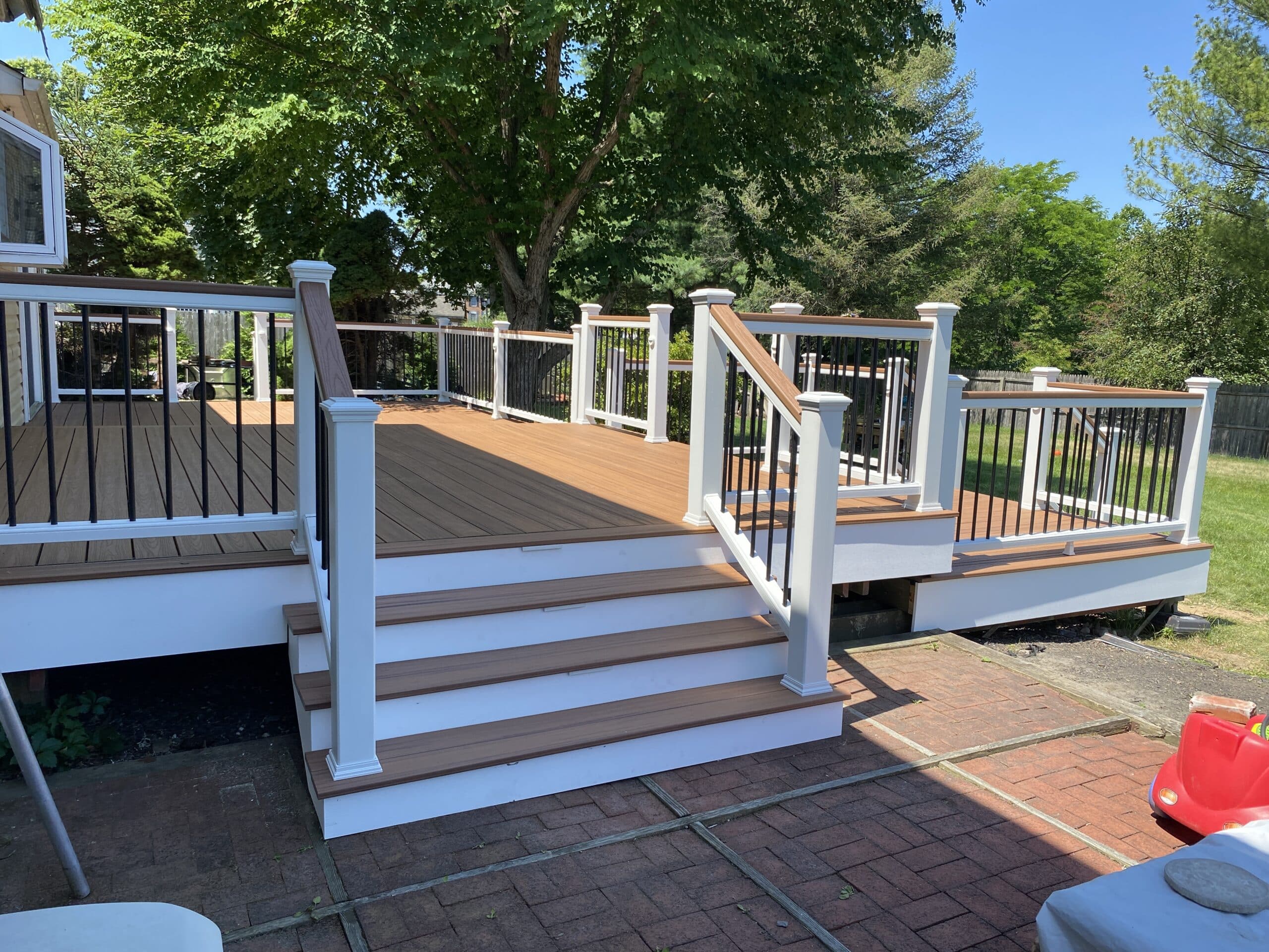 multi-level deck with white deck posts, wood-grain composite top rail, and black balusters