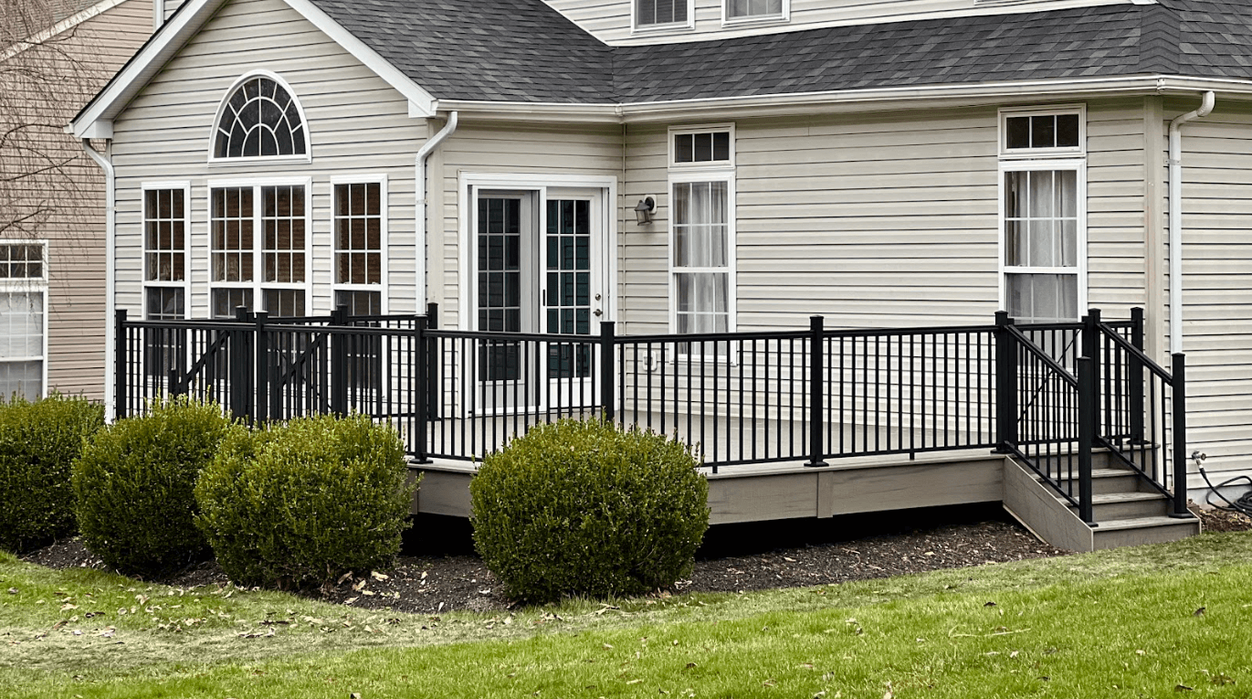 An elevated outdoor deck with black metal railings, gray decking, and steps leading to a grassy yard, attached to a beige house with large windows - Metal Deck Railing Ideas - Railings for decks