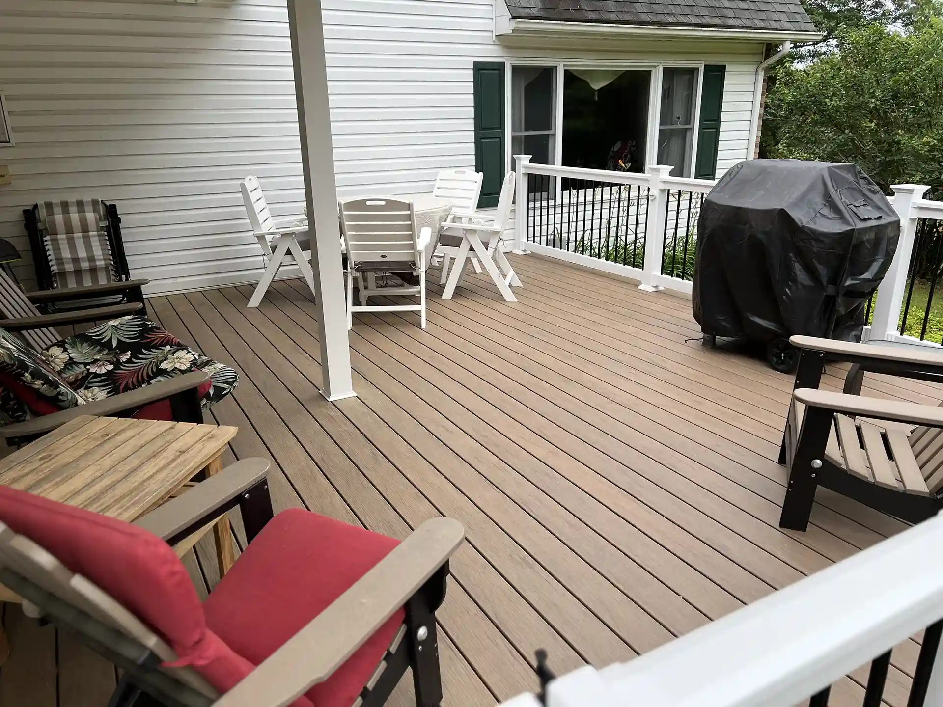 Backyard composite deck with white railing, outdoor furniture, and a covered grill attached to a suburban home.