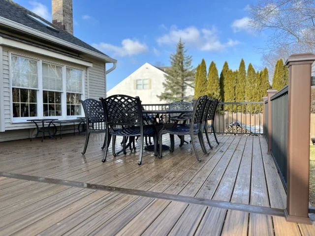 Outdoor composite deck with black wrought iron patio furniture attached to a suburban home.