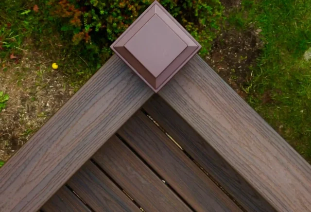 Close-up of a composite deck corner with a brown post cap and wood-textured boards.