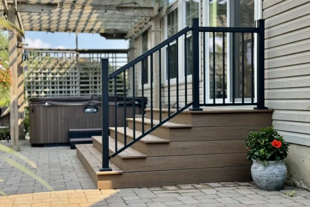 A set of stairs leading to a deck, with black railings and composite wood steps, next to a hot tub and a potted plant.