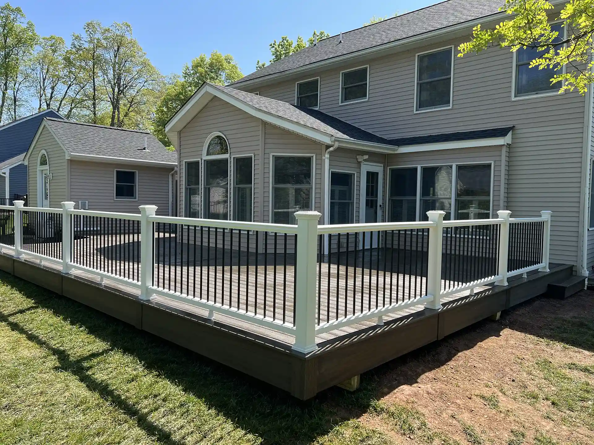 A spacious backyard deck with white railings and black balusters, attached to a two-story house. 