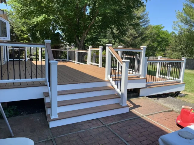 Deck with stairs, black metal railings, and white posts.