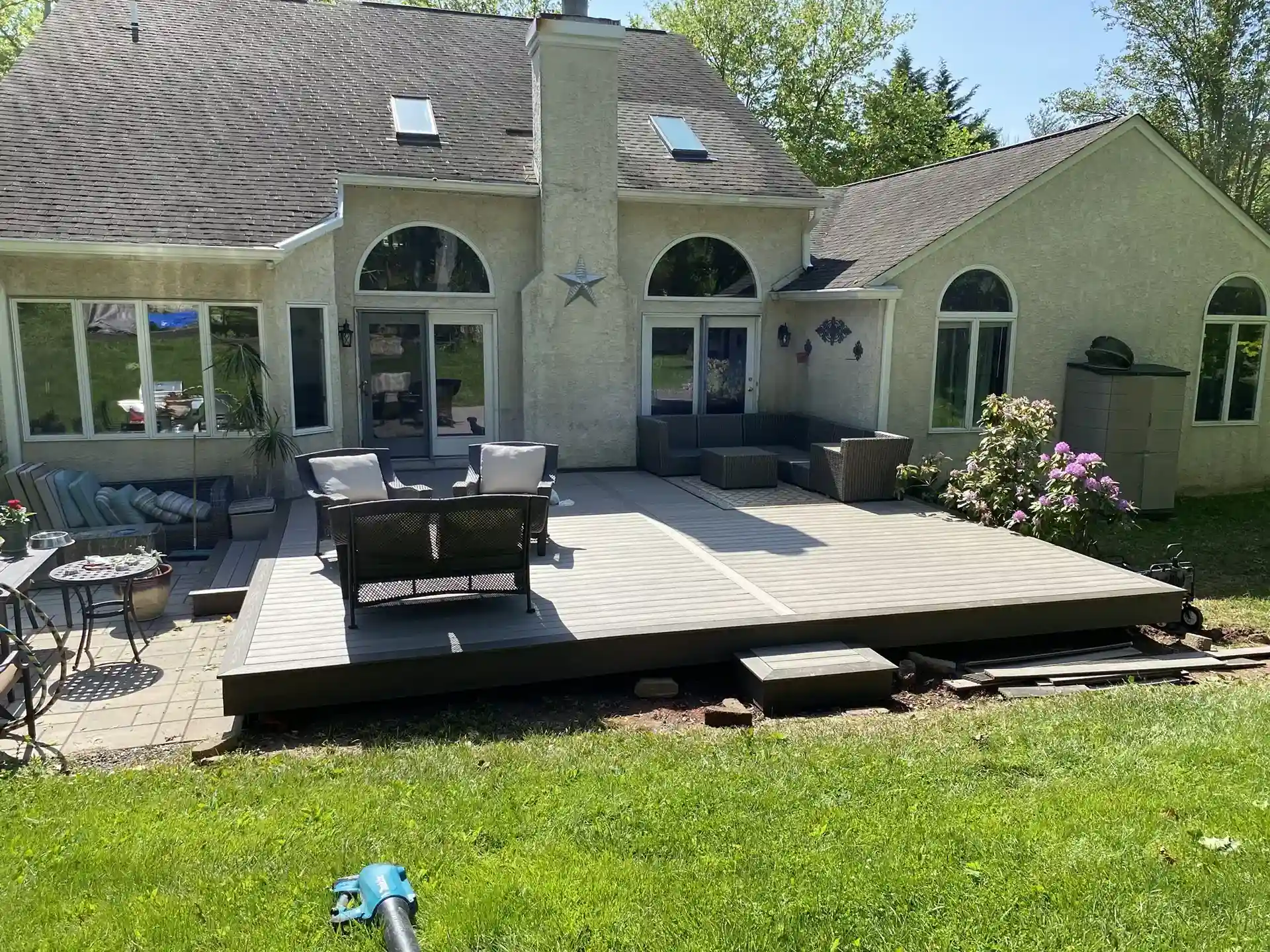 A backyard view of a light gray wooden deck extending from a house with a stucco exterior. 
