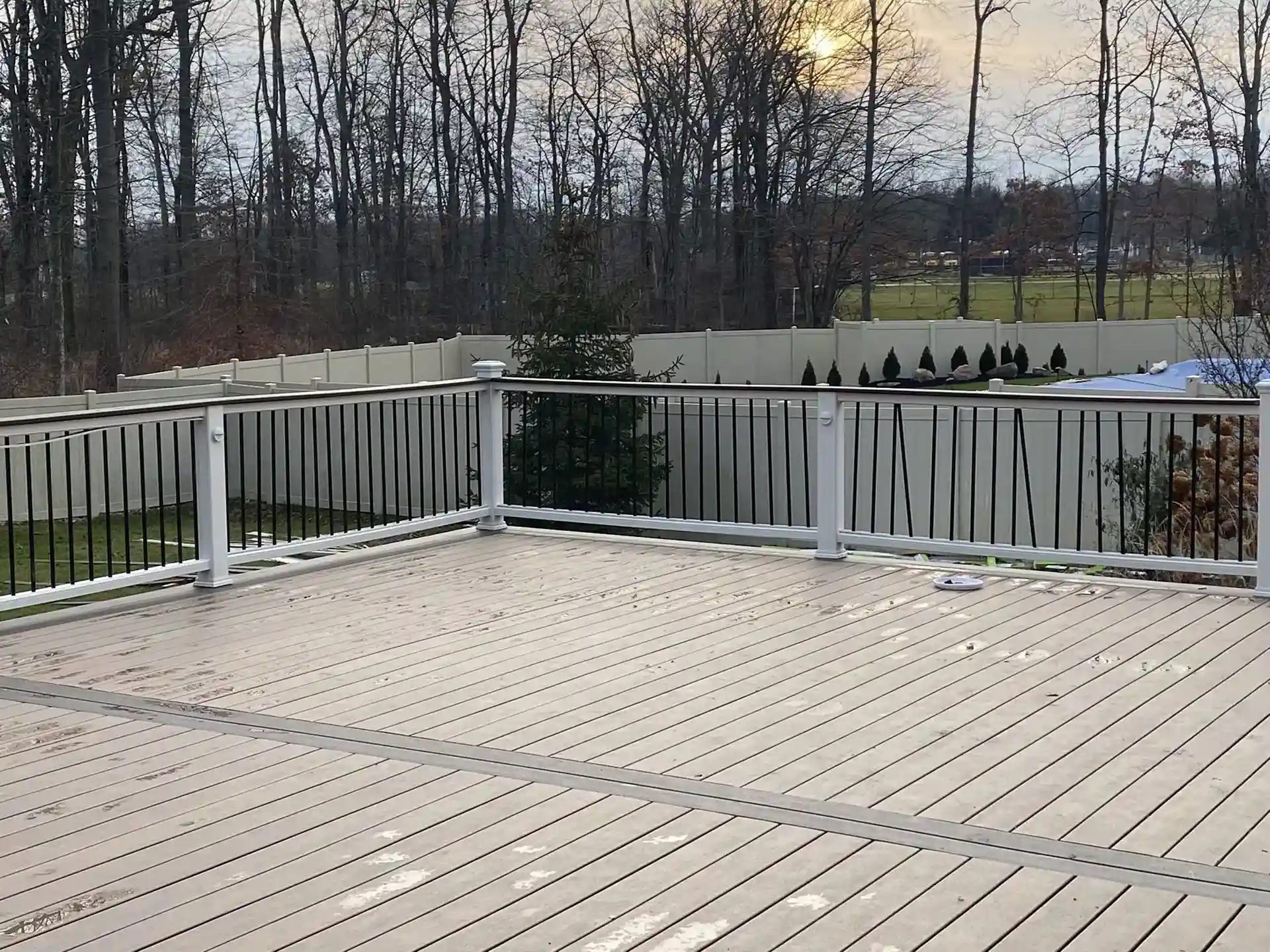 A low-angle shot shows a wet, light gray wooden deck enclosed by a white vinyl railing with black aluminum balusters. 