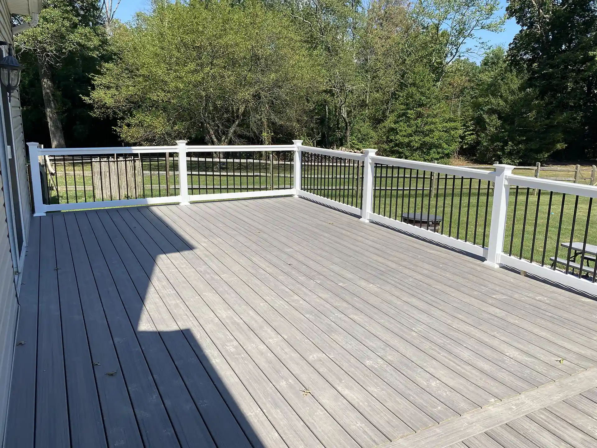 Spacious composite deck with white and black railing, overlooking a lush backyard. 