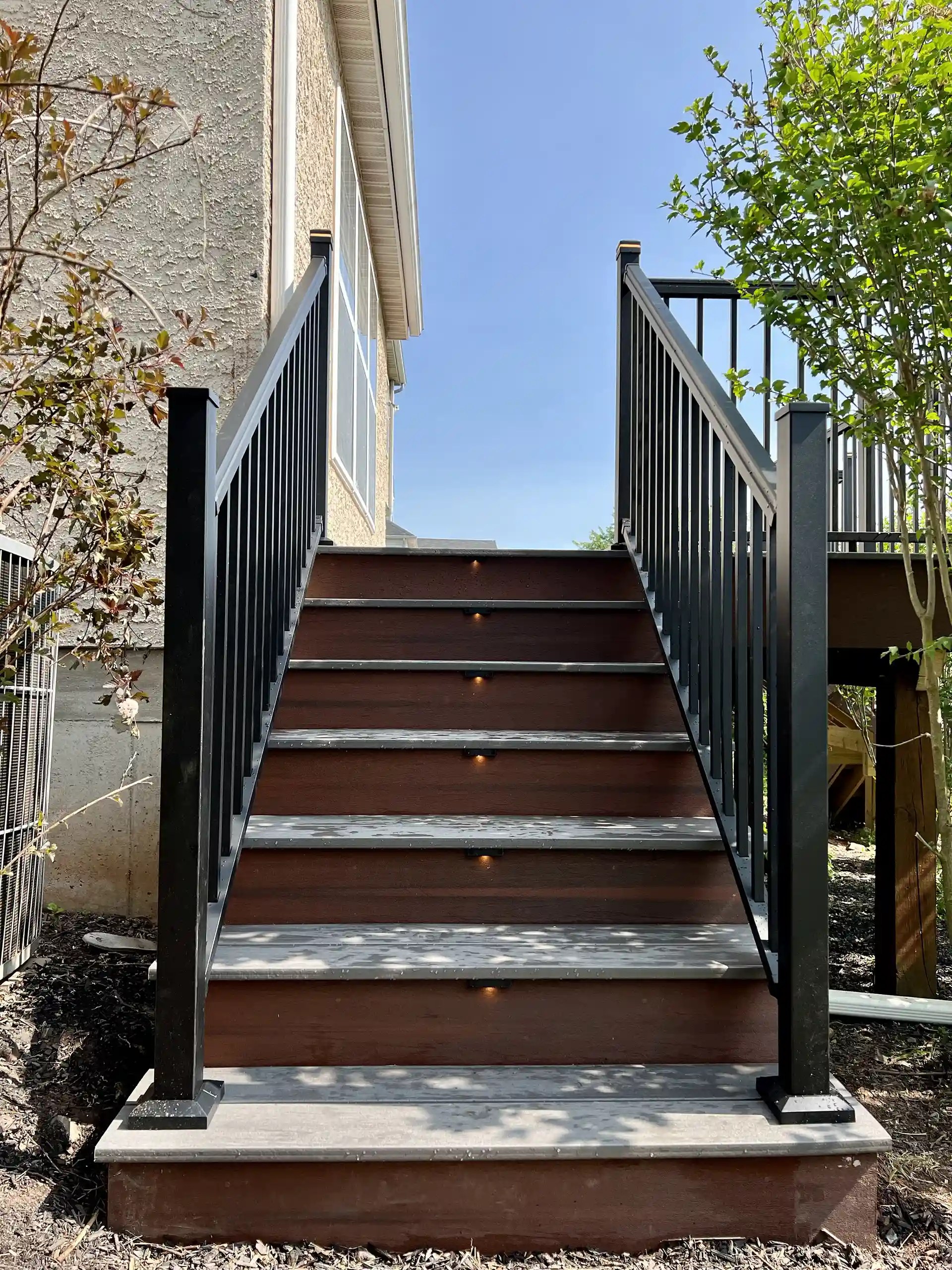 Modern outdoor deck staircase with composite steps, black railings, and integrated step lighting. 